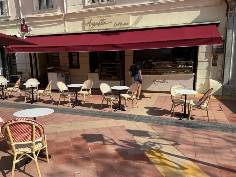 Façade d'Augustin Menton avec son store bordeaux, son comptoir en marbre et sa terrasse aux chaises cannées, place Georges Clémenceau