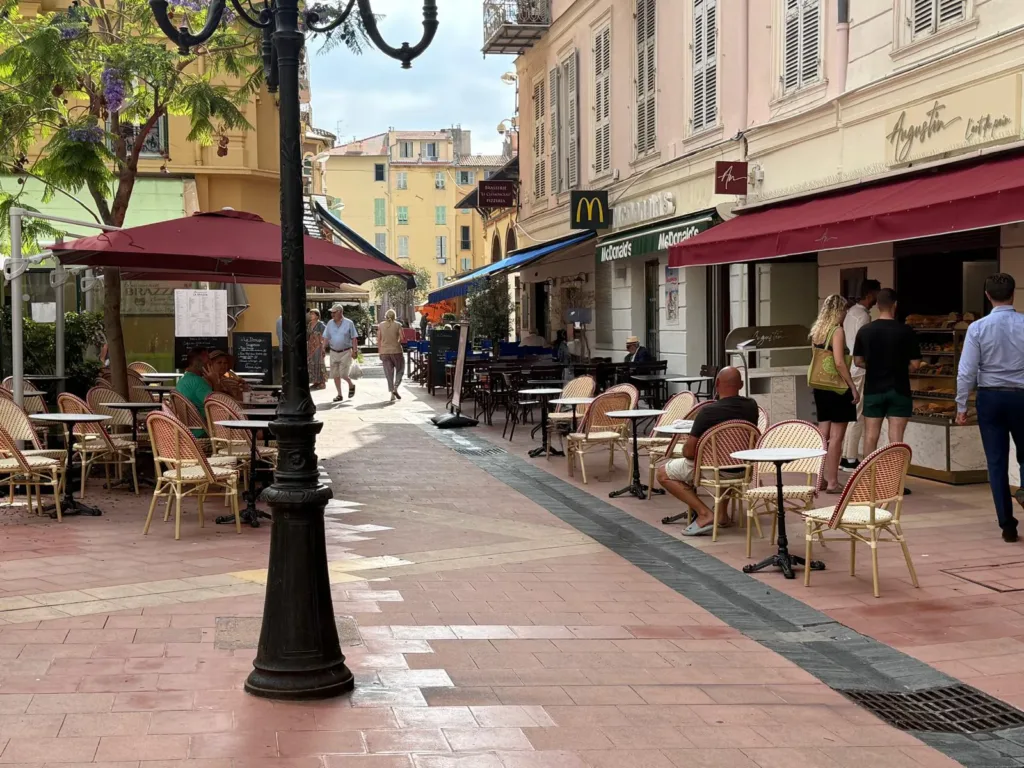 Rue piétonne du centre-ville de Menton avec la boutique Augustin, son store bordeaux et sa terrasse