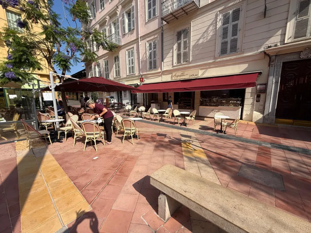 Terrasse d'Augustin Menton sur la place Georges Clémenceau, avec tables en marbre et chaises cannées bordeaux et crème