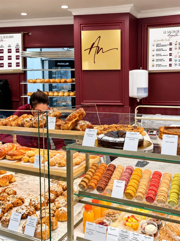 Macarons colorés, brioches, viennoiseries et pâtisseries en vitrine à Augustin Paris Convention, devant le monogramme doré d'Augustin